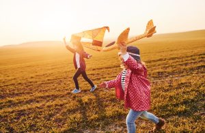 Two little girls friends have fun together with kite and toy plane on the field at sunny daytime.