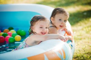 The two Two-year old little baby girls playing with toys in inflatable pool in the summer sunny day