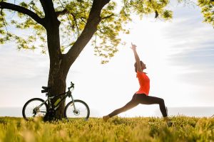 slim beautiful woman silhouette doing sports in morning in park doing yoga on mat in colorful fitness outfit in nature, smiling happy healthy lifestyle, calm meditation, bicycle on background