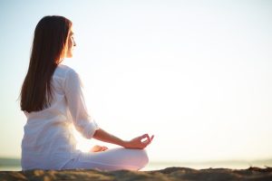 Side view of meditating woman sitting in pose of lotus against clear sky outdoors