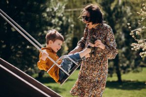 Mother with her little son swinging on the backyard